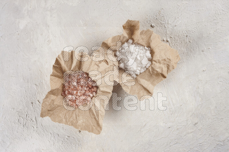 2 crumpled pieces of paper full of pink himalayan salt and white salt on white background