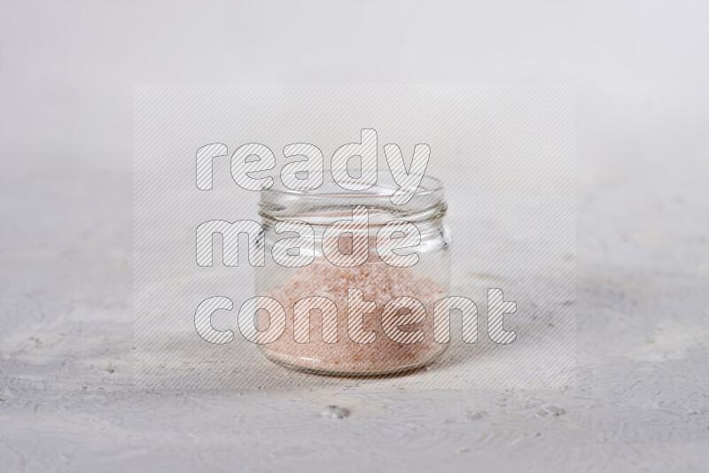 A glass jar full of fine himalayan salt on white background