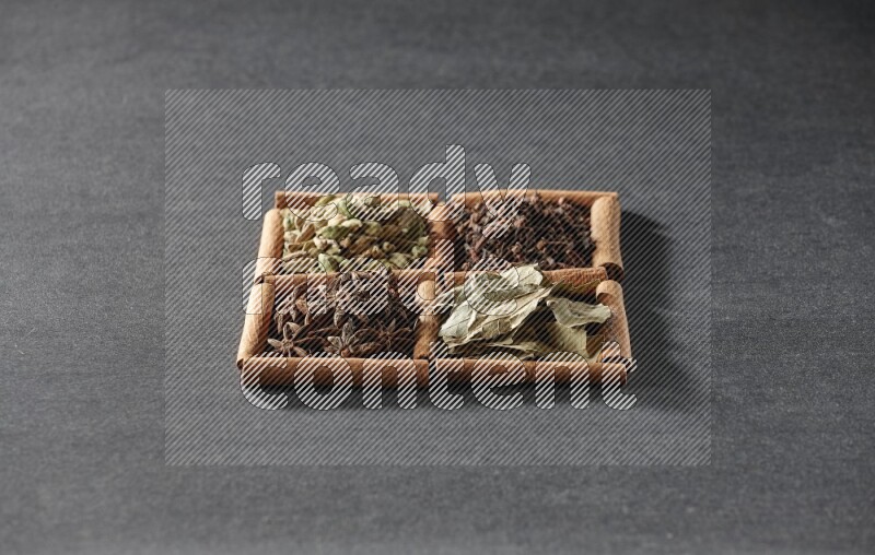 4 squares of cinnamon sticks full of star anise, cardamom, cloves and bay laurel leaves on black flooring
