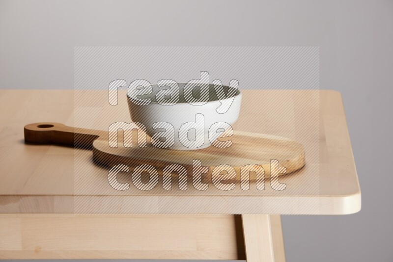 grey bowl placed on a  wooden oval cutting board on the edge of wooden table