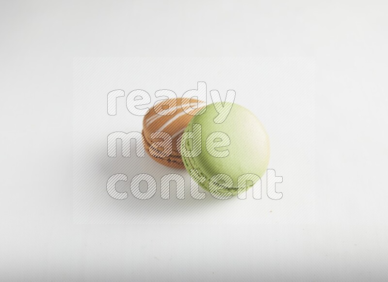 45º Shot of of two assorted Brown Irish Cream, and Green Pistachio macarons on white background