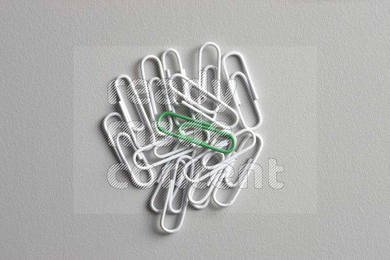 A bunch of white paper clips with a different colored paper clip in the center on grey background