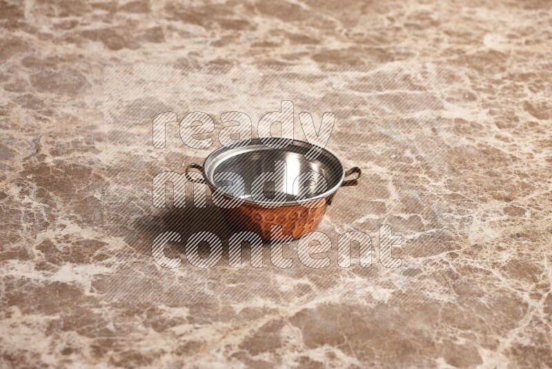 A small copper pot on beige marble background