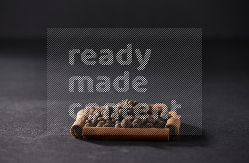 A single square of cinnamon sticks full of allspice on black flooring
