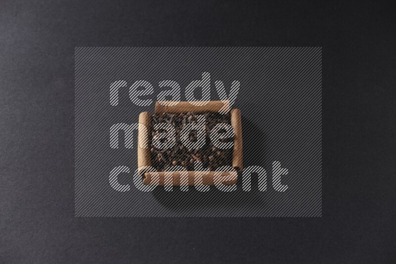 A single square of cinnamon sticks full of cloves on black flooring