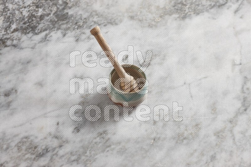 Multicolored pottery bowl with wooden honey dipper in it on grey marble background