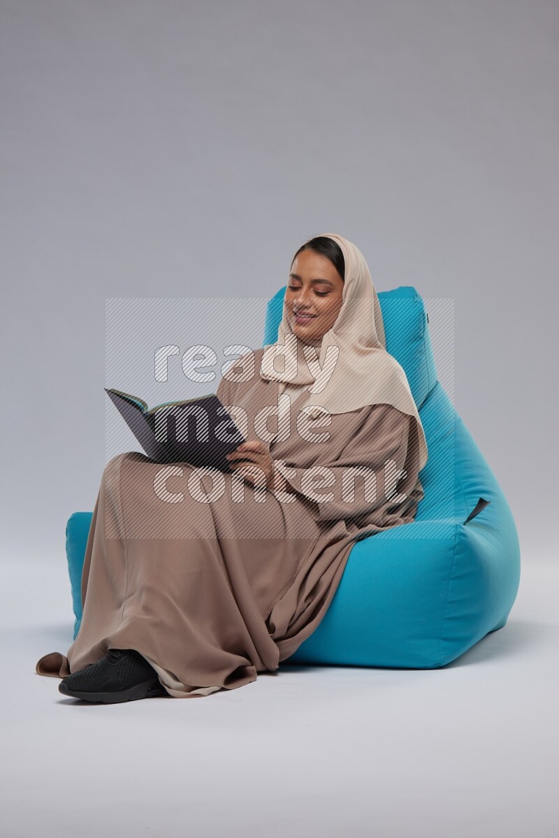 A woman sitting on a blue beanbag and reading a book