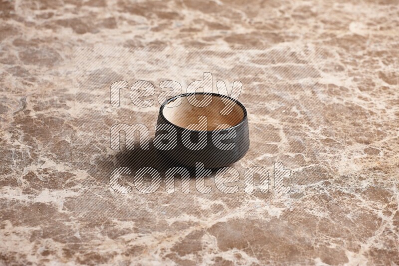 A black pottery bowl on beige marble background