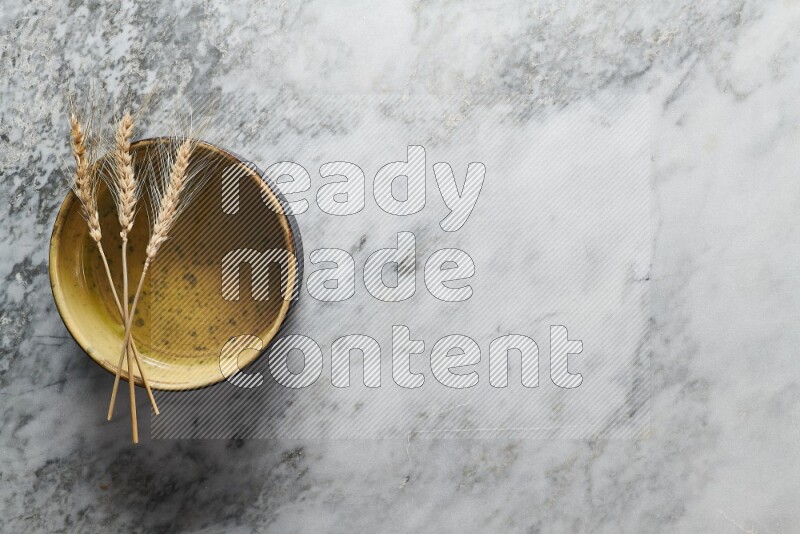 Wheat stalks on multicolored pottery oven plate on grey marble background