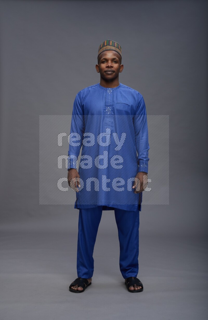 Man wearing Nigerian outfit standing interacting with the camera on gray background