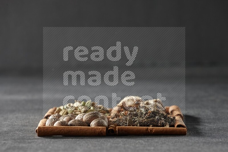 4 مربعات من عيدان القرفة ممتلئة بالريحان المجفف والهيل والزنجبيل المجفف وجوزة الطيب على أرضية سوداء