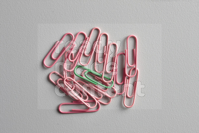 A bunch of pink paper clips with a different colored paper clip in the center on grey background