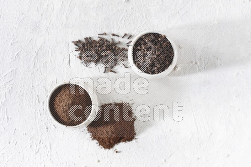 2 Beige ceramic bowls, one full of cloves and the other full of powder on textured white flooring