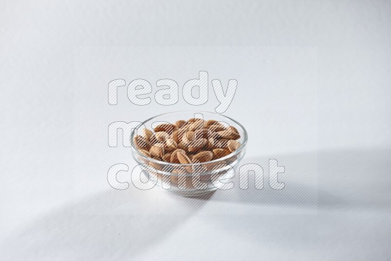A glass bowl full of peeled almonds on a white background in different angles