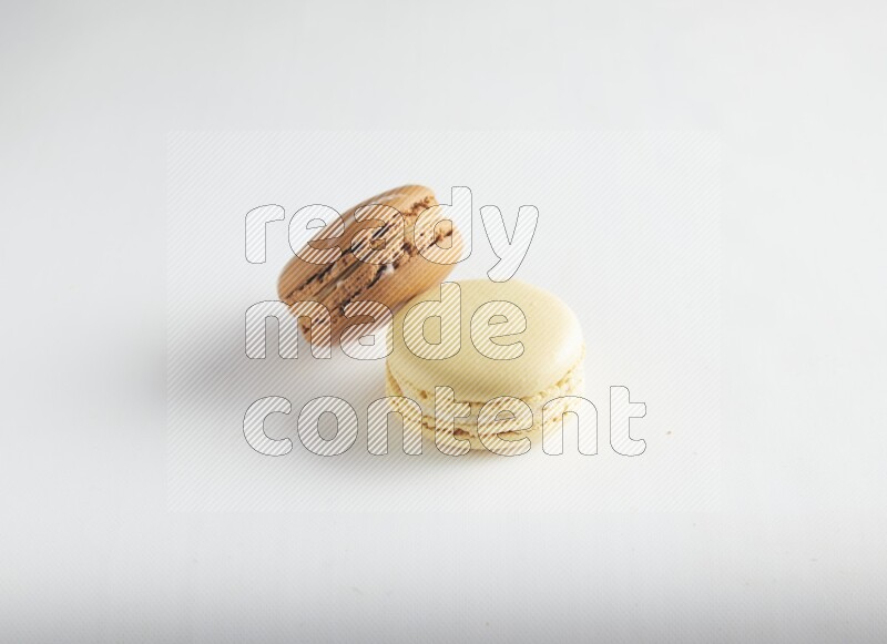 45º Shot of of two assorted Brown Irish Cream, and Yellow Vanilla macarons on white background