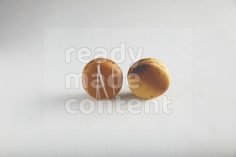 45º Shot of of two assorted Brown Irish Cream, and Yellow Crème Brulée macarons on white background