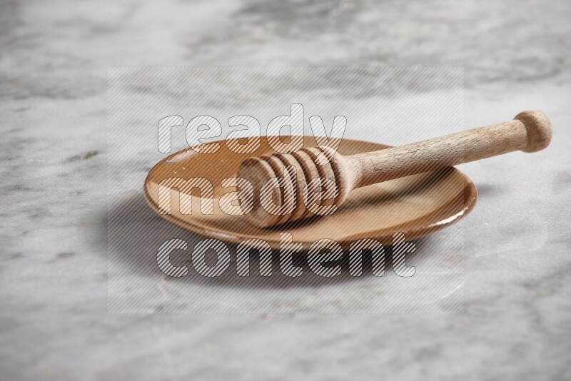 Multicolored pottery plate with wooden honey dipper in it on grey marble background