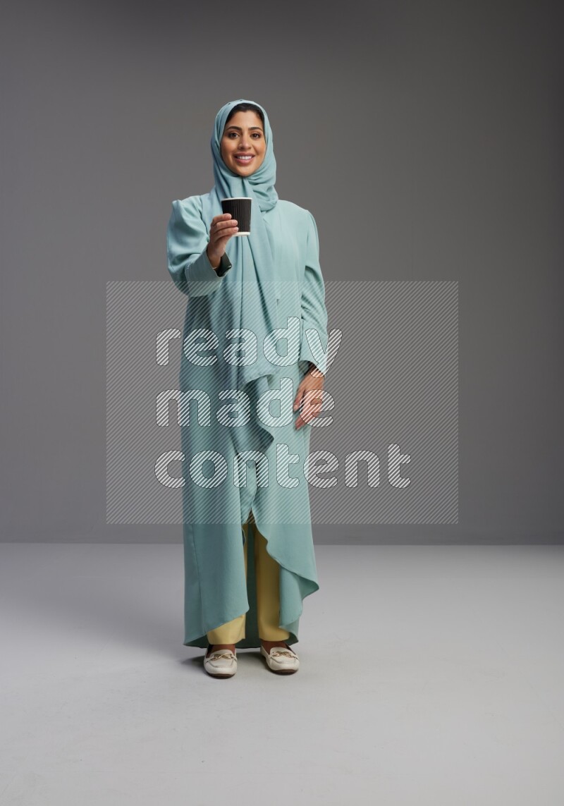 Saudi Woman wearing Abaya standing  holding paper cup on Gray background
