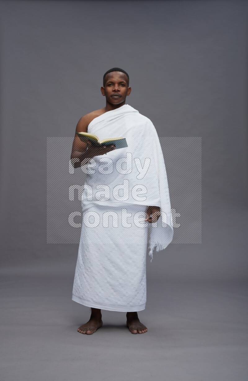A man wearing Ehram Standing reading quran on gray background