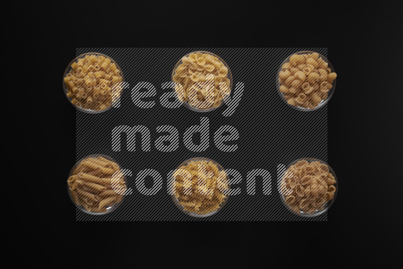 Different pasta types in 6 glass bowls on black background