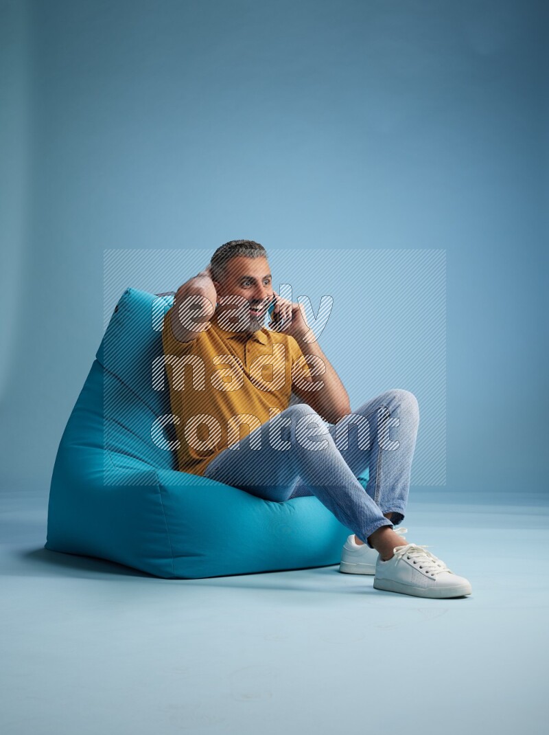A man sitting on a blue beanbag and talking on the phone