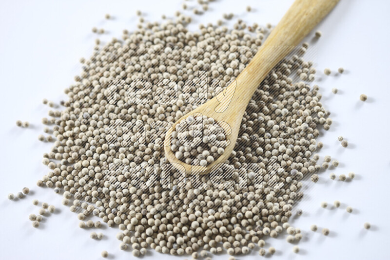 White pepper beads with wooden spoon on white background