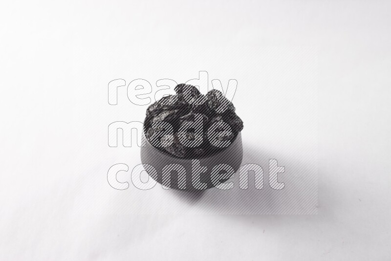 Dried plums in a black pottery bowl on white background