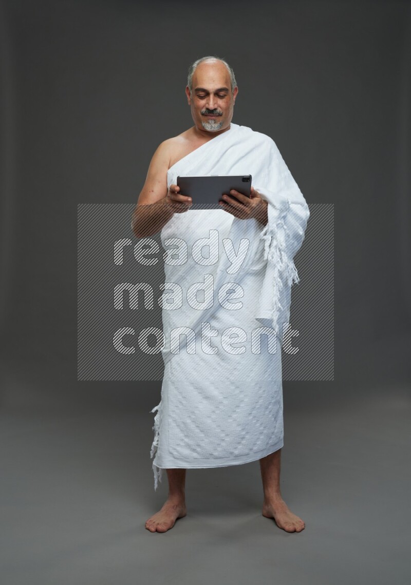 A man wearing Ehram Standing working on tablet on gray background