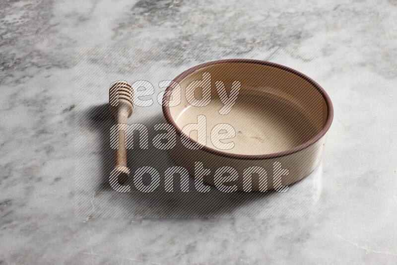 Beige pottery oven bowl with wooden honey dipper on the side on grey marble background