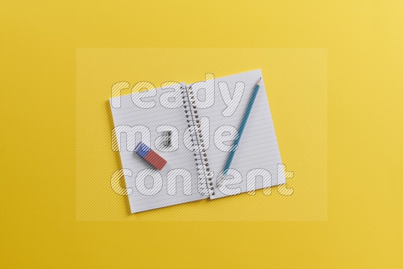 An open notebook with different school supplies on yellow background