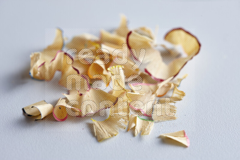 A close-up showing a small pile of pencil shavings with varied color edges on grey background