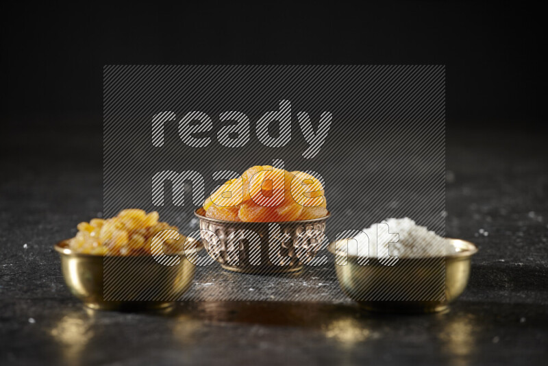 Dried fruits in metal bowls in a dark setup