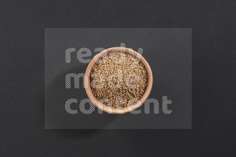 A wooden bowl full of mustard seeds on a black flooring