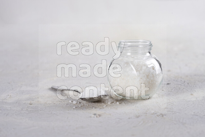 A glass jar full of coarse sea salt crystals on white background