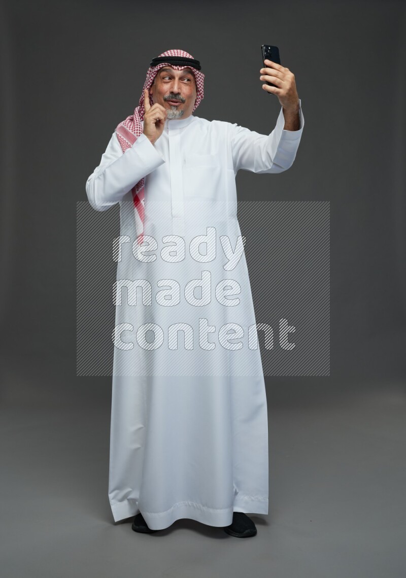 Saudi man with shomag Standing taking selfie on gray background