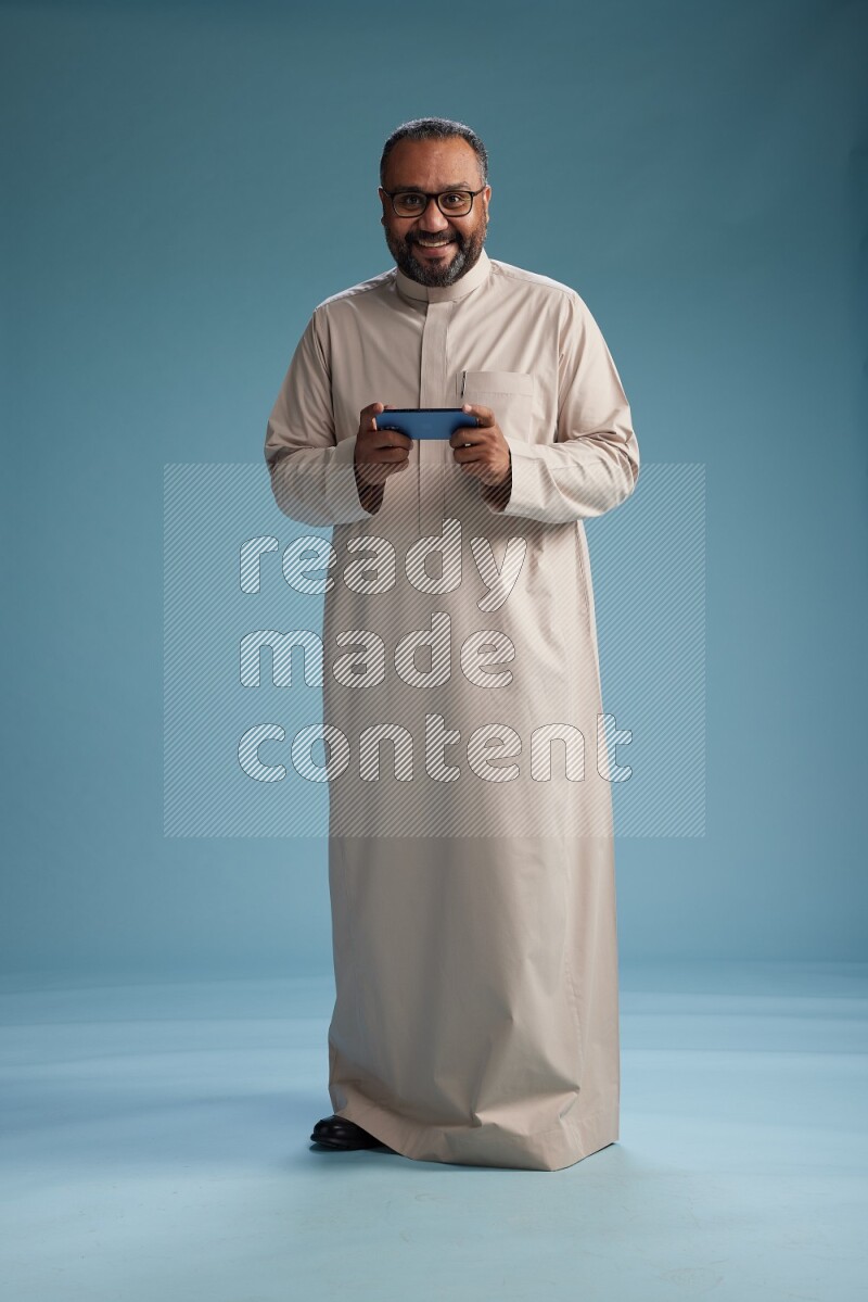 Saudi Man without shimag Standing texting on phone on blue background