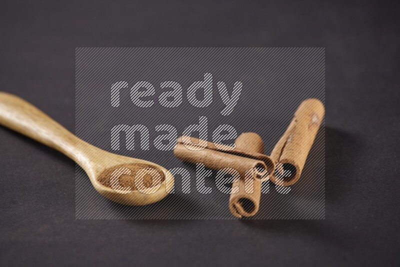 3 Cinnamon sticks stacked beside a wooden spoon full of cinnamon powder on black background in different angles