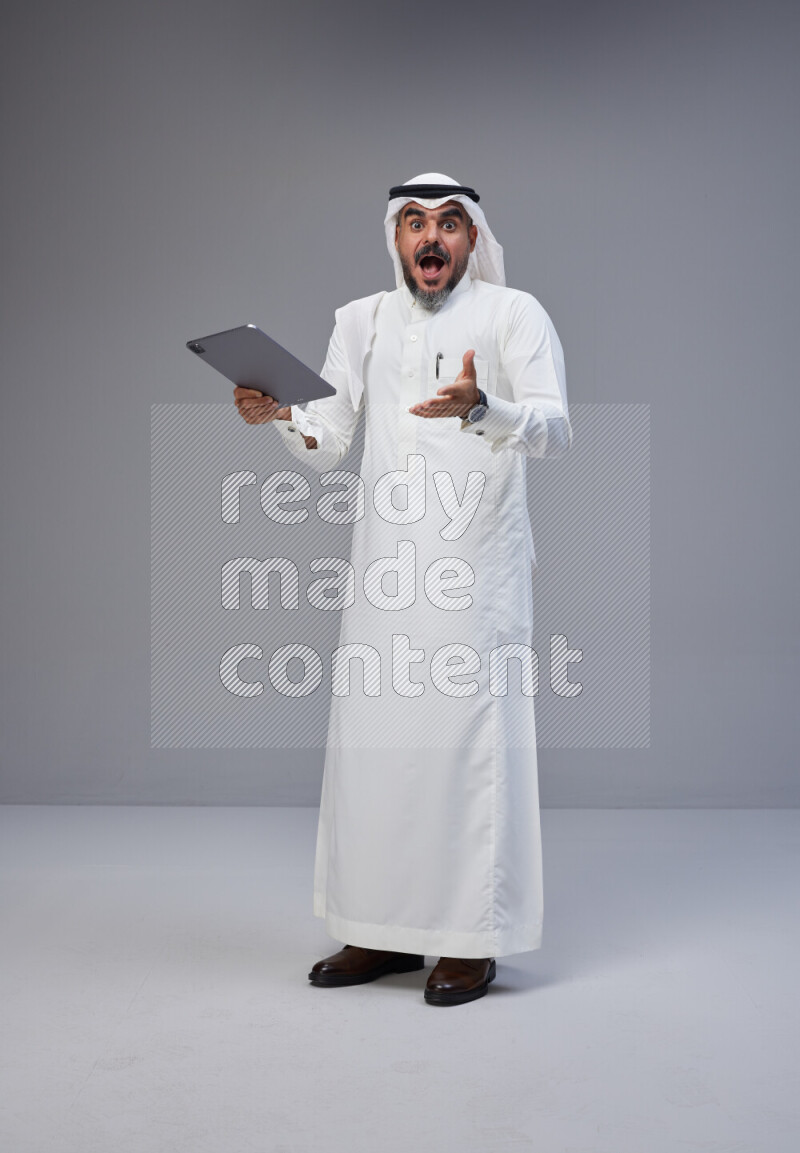 Saudi man Wearing Thob and white Shomag standing working on tablet on Gray background