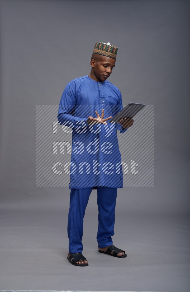 Man wearing Nigerian outfit standing working on tablet on gray background