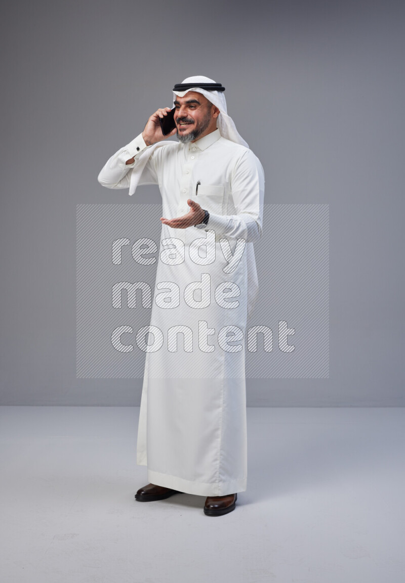Saudi man Wearing Thob and white Shomag standing talking on phone on Gray background