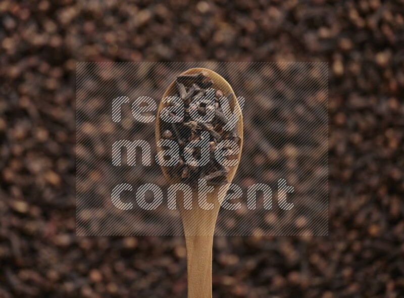 A wooden spoon full of cloves on cloves background and black flooring