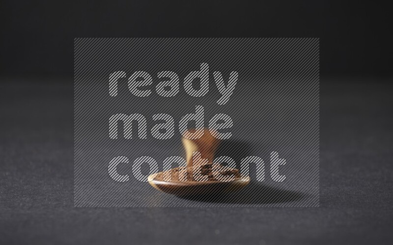 A wooden ladle full of cloves powder on a black flooring