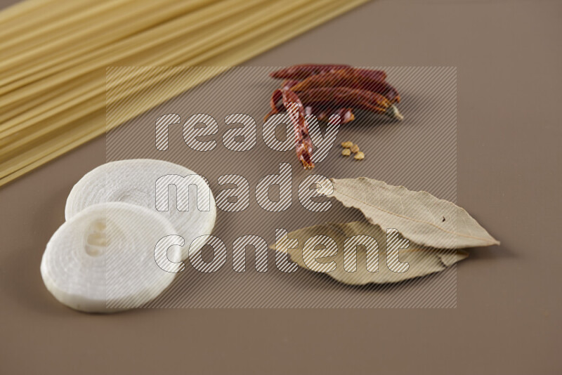 Raw pasta with different ingredients such as cherry tomatoes, garlic, onions, red chilis, black pepper, white pepper, bay laurel leaves, rosemary and cardamom on beige background
