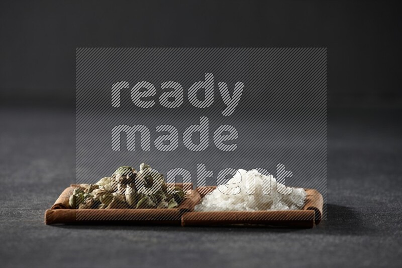 2 squares of cinnamon sticks full of white salt and cardamom on black flooring