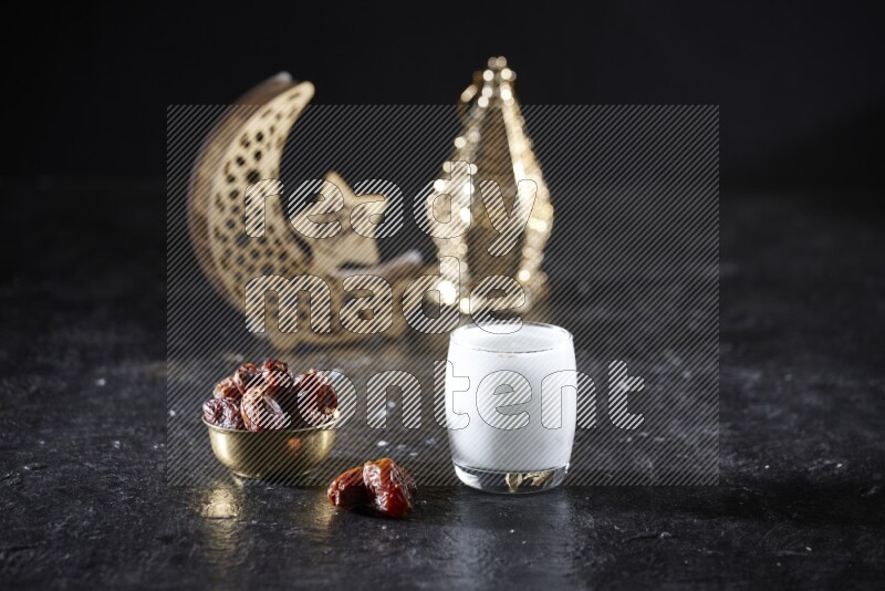 Dates in a metal bowl with sobia beside golden lanterns in a dark setup