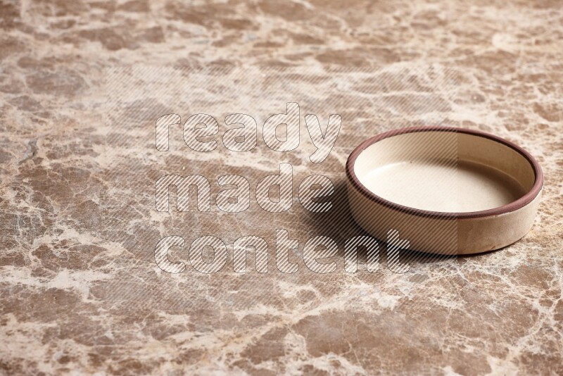 A beige pottery oven plate on beige marble background