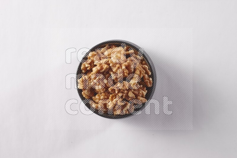 Walnuts in a black pottery bowl on white background