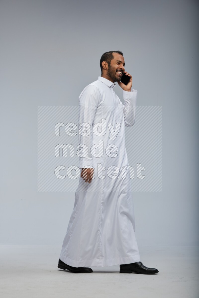 Saudi man wearing Thob standing talking on phone on Gray background