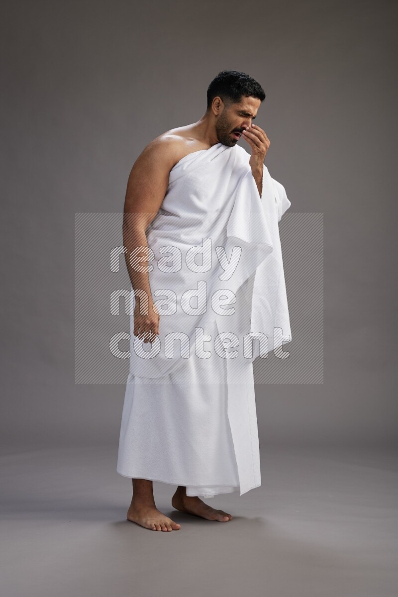 A man wearing Ehram standing showing how to sneeze on gray background