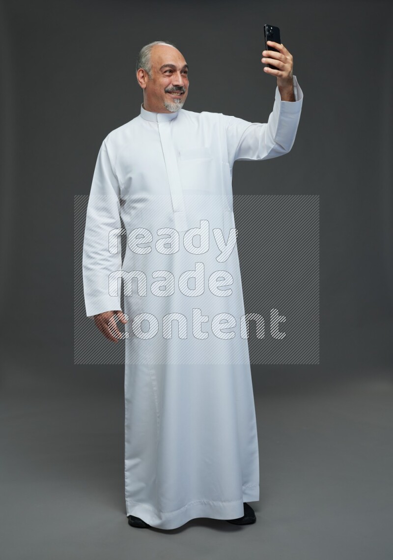 Saudi man without shomag Standing taking selfie on gray background